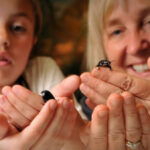 A woman and a child smile while handling small black bugs.